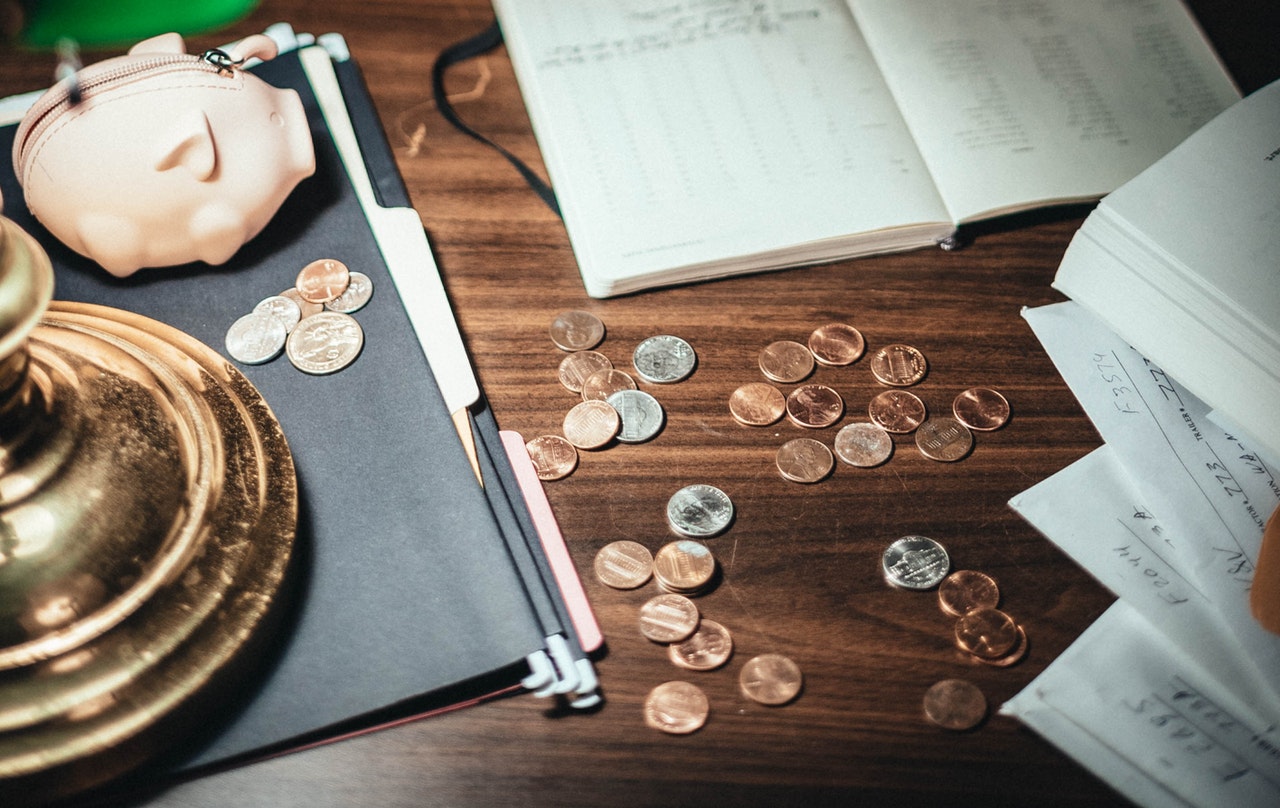 Wooden table covered in coins, a notebook, and small piggy bank