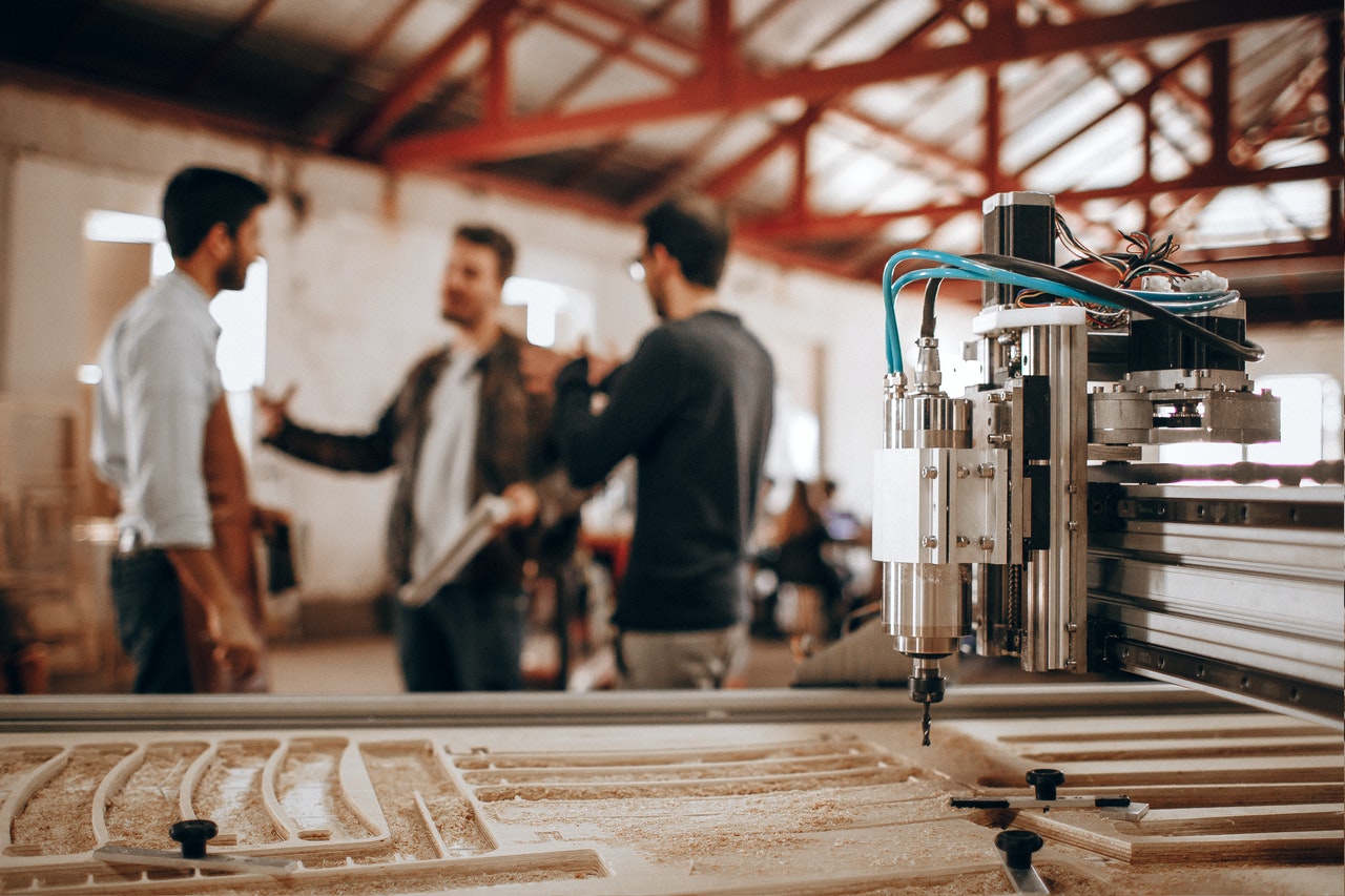 Three business men talking in background behind large industrial machine.